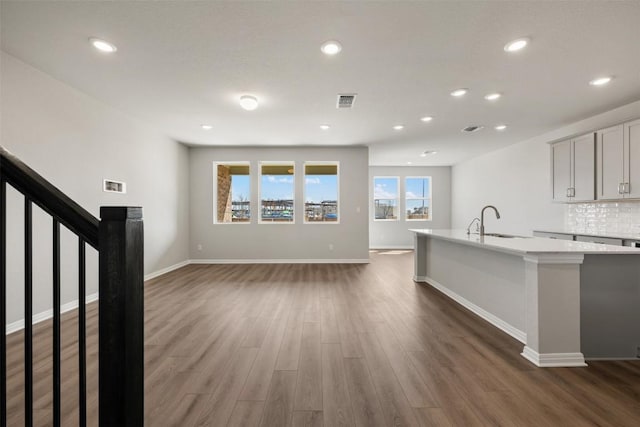 kitchen featuring dark wood-style floors, visible vents, decorative backsplash, a sink, and an island with sink