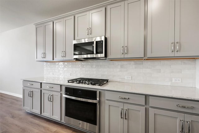 kitchen with light stone counters, stainless steel appliances, gray cabinets, light wood-style flooring, and decorative backsplash