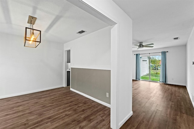 empty room with dark hardwood / wood-style flooring and ceiling fan with notable chandelier