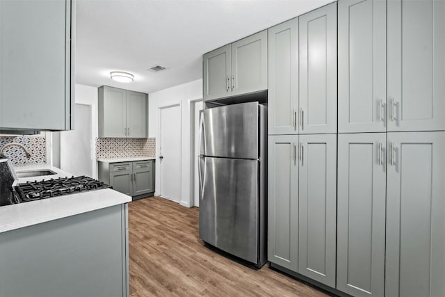 kitchen with gray cabinets, stainless steel refrigerator, sink, decorative backsplash, and light wood-type flooring