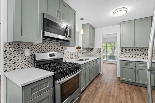 kitchen with sink, appliances with stainless steel finishes, hanging light fixtures, light hardwood / wood-style floors, and decorative backsplash