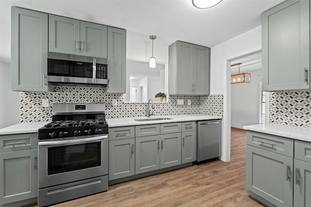 kitchen featuring appliances with stainless steel finishes, pendant lighting, sink, backsplash, and light hardwood / wood-style flooring