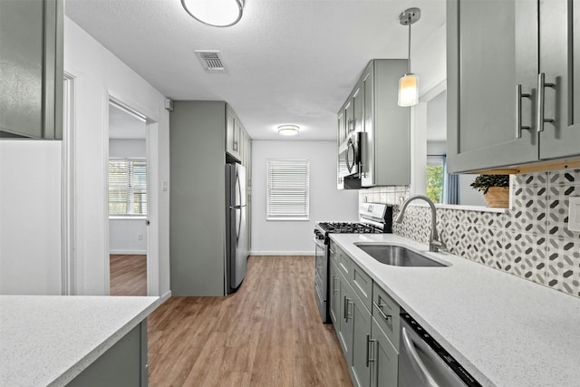 kitchen with appliances with stainless steel finishes, pendant lighting, sink, gray cabinetry, and decorative backsplash