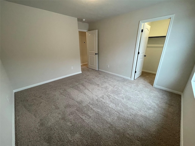 unfurnished bedroom with a walk in closet, a closet, and carpet flooring