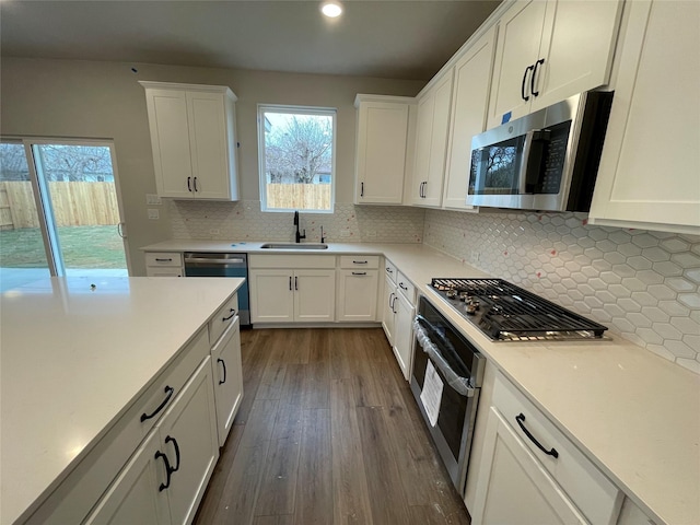 kitchen with appliances with stainless steel finishes, decorative backsplash, dark hardwood / wood-style flooring, white cabinets, and sink