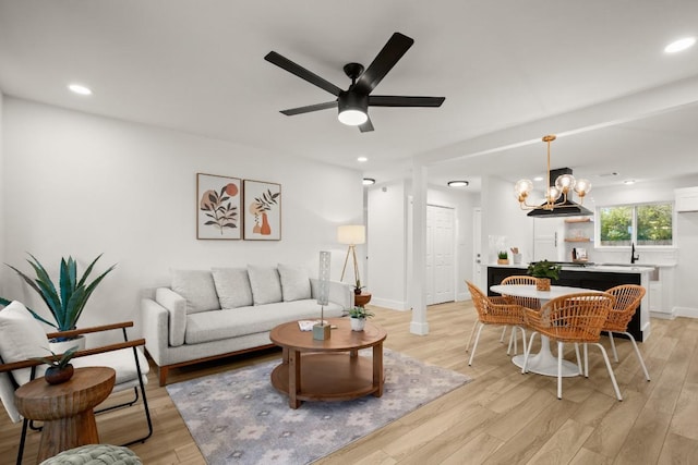 living room featuring ceiling fan with notable chandelier and light wood-type flooring