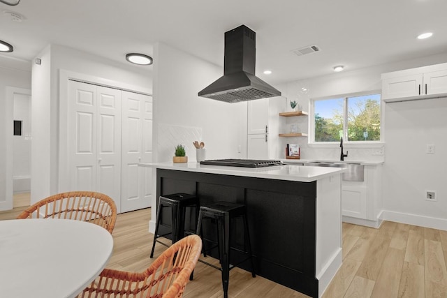 kitchen featuring island exhaust hood, light wood-type flooring, a breakfast bar, white cabinetry, and stainless steel gas stovetop