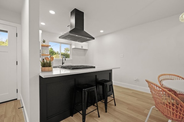 kitchen with kitchen peninsula, a kitchen bar, island range hood, and white cabinetry