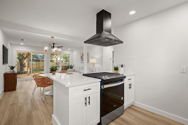 kitchen featuring stainless steel gas stove, wall chimney range hood, kitchen peninsula, white cabinets, and light wood-type flooring