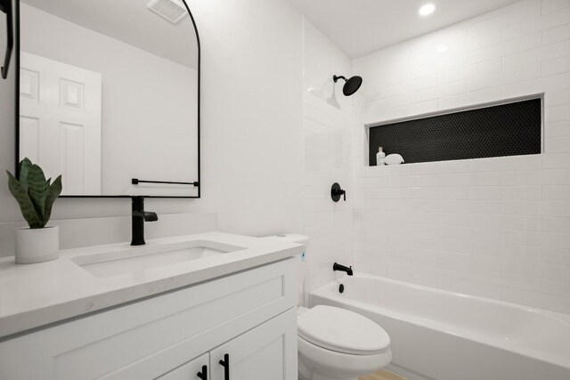 full bathroom with tiled shower / bath, vanity, and toilet