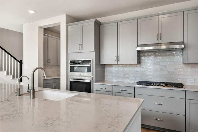 kitchen featuring sink, appliances with stainless steel finishes, gray cabinetry, light stone counters, and decorative backsplash