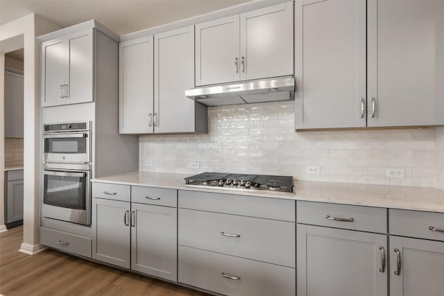 kitchen featuring hardwood / wood-style flooring, gray cabinets, decorative backsplash, and appliances with stainless steel finishes