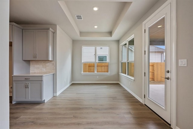 kitchen featuring backsplash, gray cabinets, a raised ceiling, and light wood-type flooring