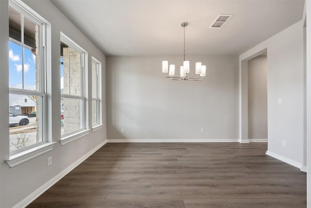 spare room with dark wood-type flooring and an inviting chandelier