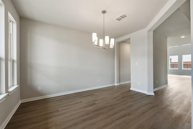 empty room featuring dark wood-type flooring and an inviting chandelier