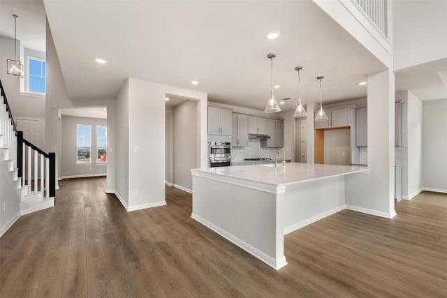 kitchen featuring pendant lighting, dark wood-type flooring, double oven, tasteful backsplash, and a wealth of natural light