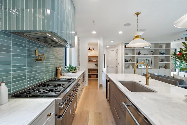 kitchen featuring sink, light hardwood / wood-style flooring, pendant lighting, stainless steel appliances, and light stone countertops