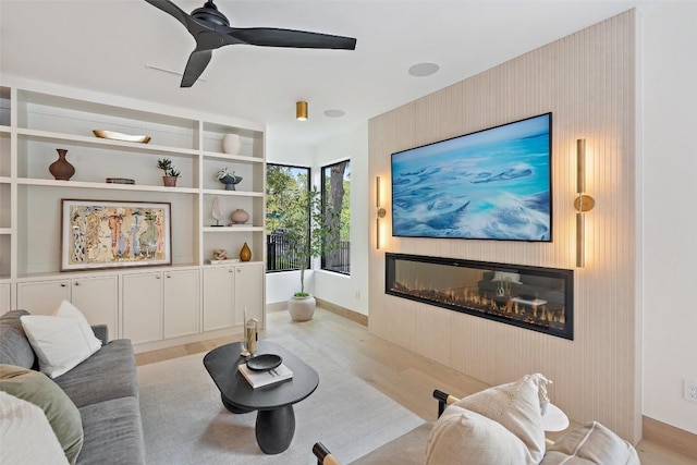 living room featuring ceiling fan, a large fireplace, and light wood-type flooring