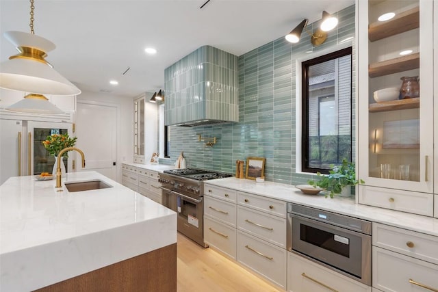 kitchen with sink, high end range, light stone countertops, white cabinets, and wall chimney exhaust hood