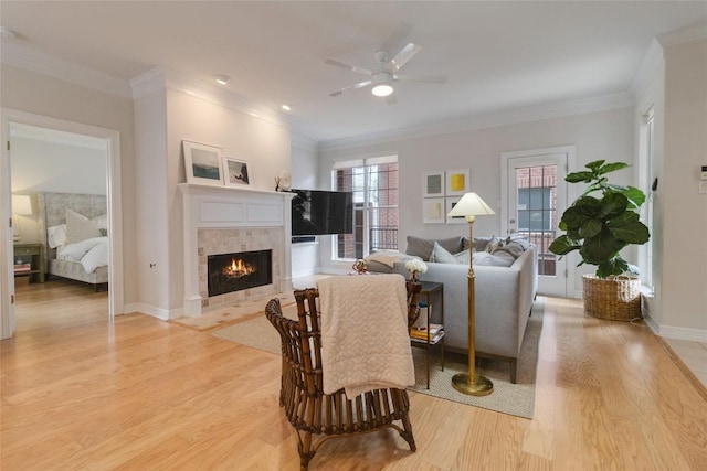 living room with a tile fireplace, ceiling fan, light hardwood / wood-style flooring, and ornamental molding