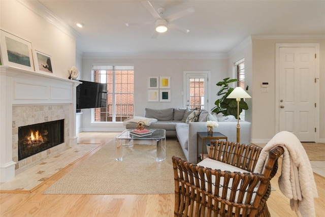 living room with a tile fireplace, ceiling fan, light hardwood / wood-style flooring, and ornamental molding