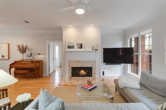 living room with ceiling fan, light hardwood / wood-style floors, ornamental molding, and a tiled fireplace