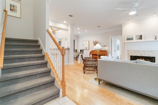 living room with ceiling fan, light hardwood / wood-style floors, ornamental molding, and a tiled fireplace