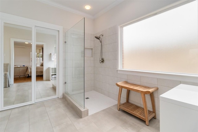 bathroom with tile patterned floors, tile walls, crown molding, and a tile shower