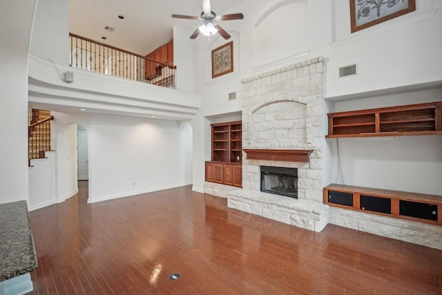 unfurnished living room featuring a fireplace, a high ceiling, ceiling fan, and dark wood-type flooring