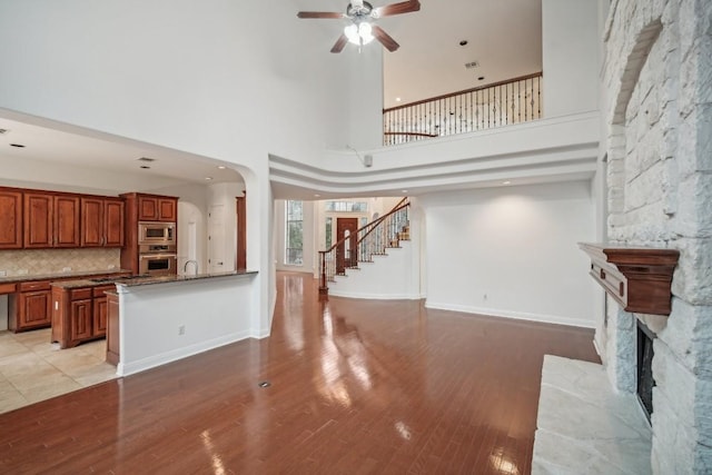 unfurnished living room featuring a stone fireplace, ceiling fan, light hardwood / wood-style flooring, and a towering ceiling