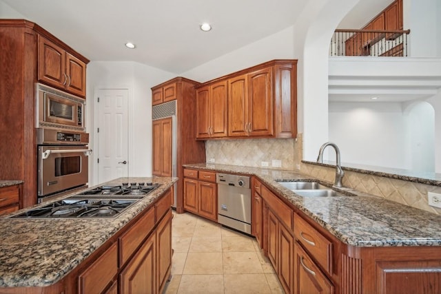 kitchen featuring kitchen peninsula, appliances with stainless steel finishes, backsplash, dark stone counters, and sink