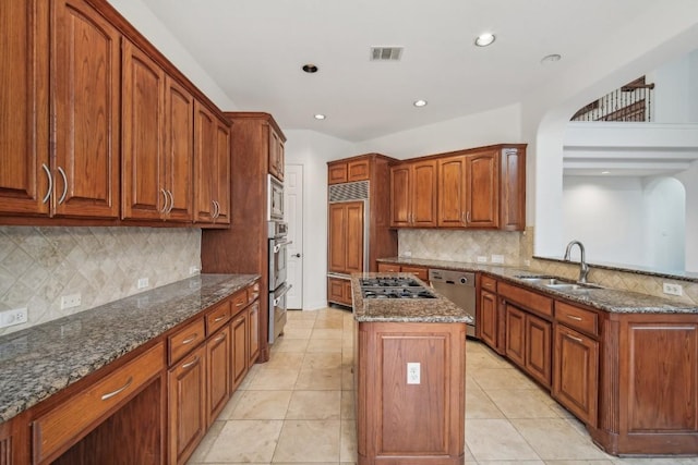 kitchen with sink, stainless steel appliances, backsplash, dark stone counters, and a kitchen island