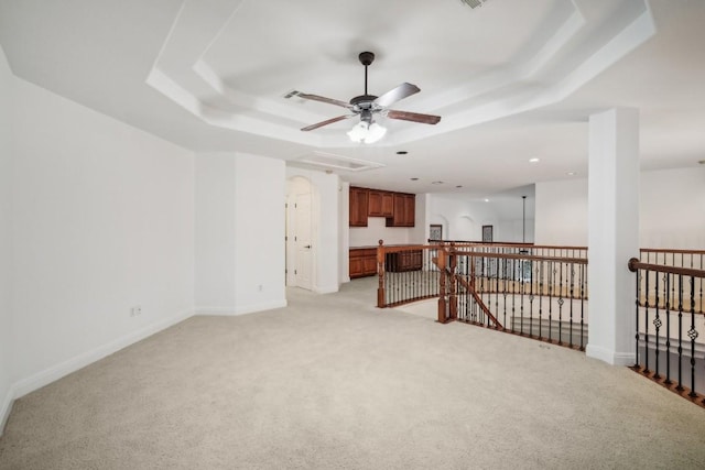 unfurnished room with ceiling fan, a raised ceiling, and light carpet