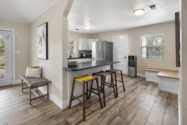 kitchen with white cabinets, a breakfast bar, a healthy amount of sunlight, and stainless steel refrigerator