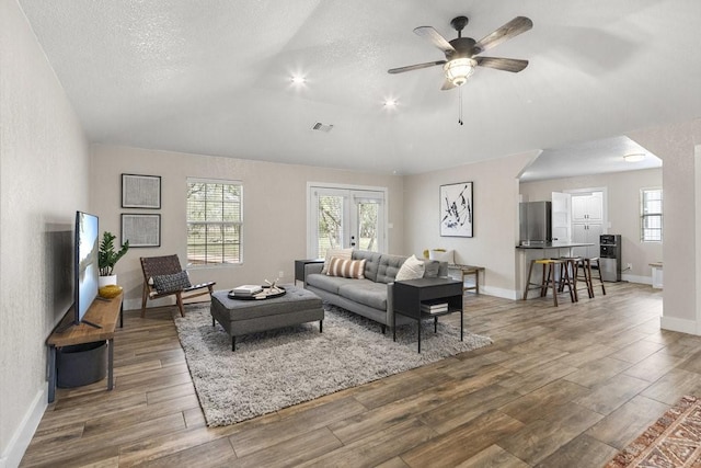 living room with hardwood / wood-style floors, a textured ceiling, vaulted ceiling, and french doors