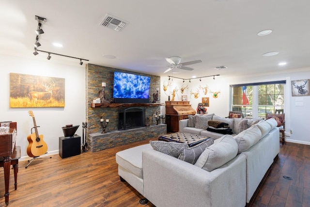 living room featuring dark wood-type flooring, a stone fireplace, rail lighting, ceiling fan, and ornamental molding