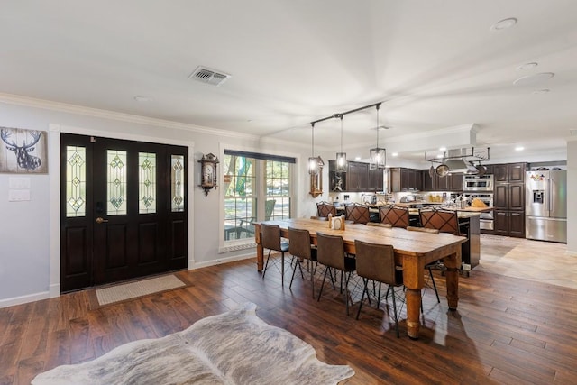 dining room with rail lighting, crown molding, and dark wood-type flooring