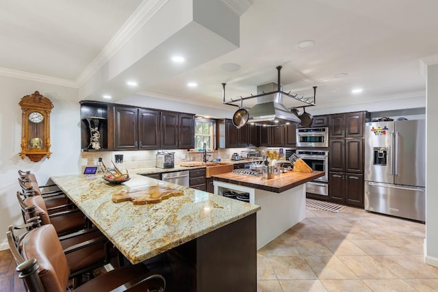 kitchen featuring dark brown cabinetry, wood counters, a kitchen breakfast bar, kitchen peninsula, and appliances with stainless steel finishes