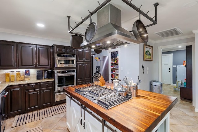 kitchen featuring wood counters, appliances with stainless steel finishes, island range hood, and ornamental molding