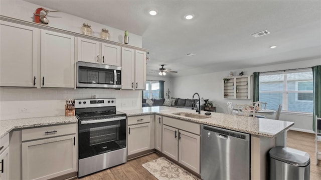 kitchen with sink, light stone countertops, kitchen peninsula, and appliances with stainless steel finishes