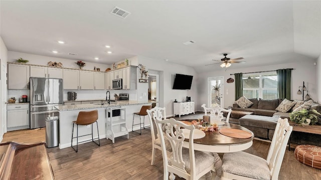 dining space with vaulted ceiling, ceiling fan, sink, and light hardwood / wood-style flooring