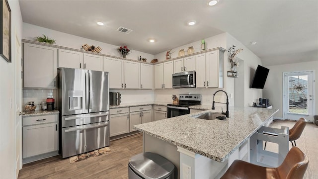 kitchen featuring sink, a breakfast bar area, gray cabinets, appliances with stainless steel finishes, and light stone counters