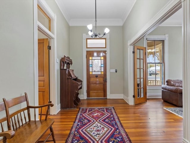 foyer entrance with wood-type flooring, ornamental molding, and a notable chandelier