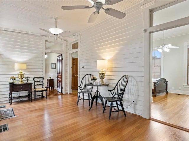 sitting room with wooden walls, crown molding, ceiling fan, and hardwood / wood-style flooring