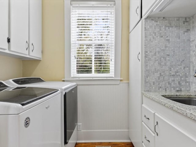 clothes washing area with cabinets, wood-type flooring, washing machine and dryer, and sink