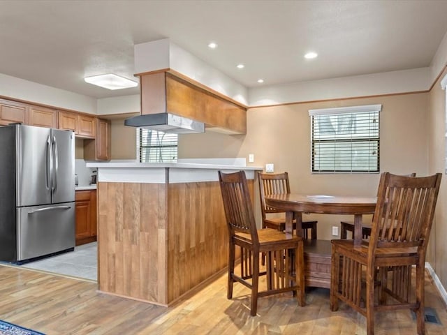 kitchen featuring a kitchen breakfast bar, kitchen peninsula, stainless steel fridge, and light wood-type flooring