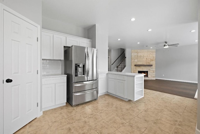 kitchen featuring ceiling fan, stainless steel refrigerator with ice dispenser, kitchen peninsula, a fireplace, and white cabinets