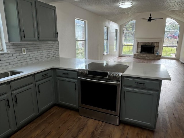 kitchen featuring kitchen peninsula, a wealth of natural light, a textured ceiling, vaulted ceiling, and stainless steel range with electric cooktop