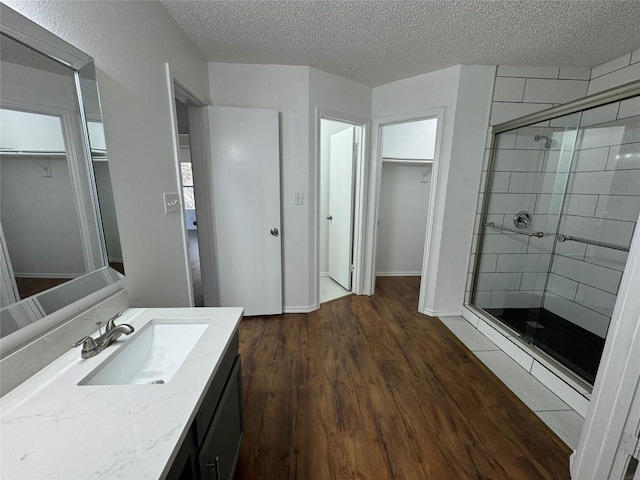 bathroom featuring hardwood / wood-style floors, vanity, a shower with shower door, and a textured ceiling