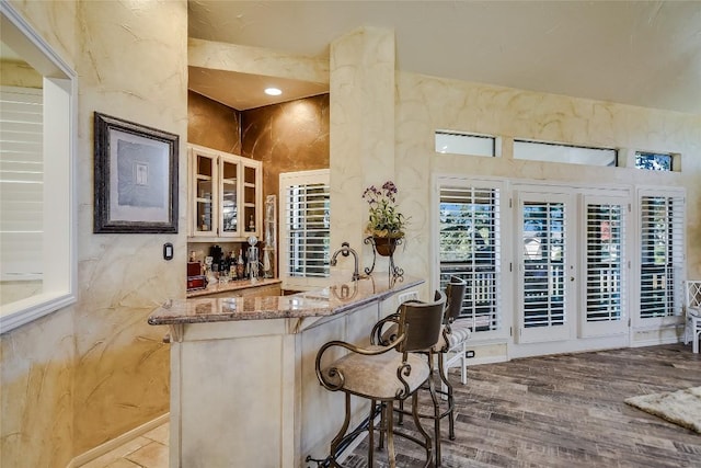 bar with light stone countertops and hardwood / wood-style flooring